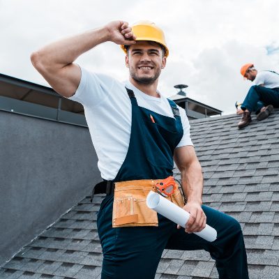 selective focus of happy repairman holding rolled paper while coworker repairing roof